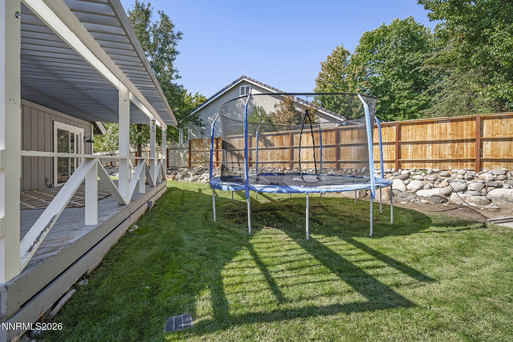 Backyard with a covered porch, lawn, trampoline, and wooden fence.
