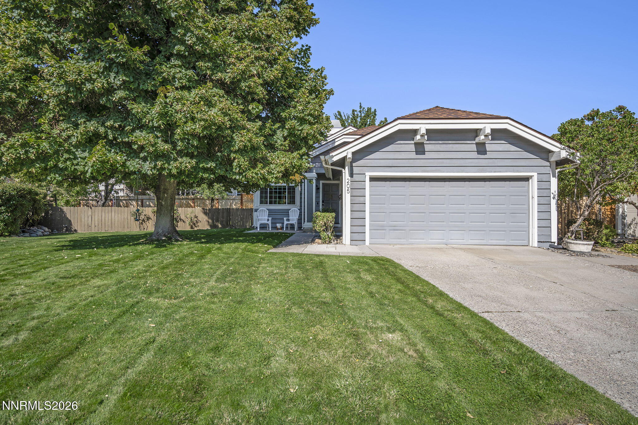 Gray single-story home with a two-car garage, broad lawn, and large shade tree.
