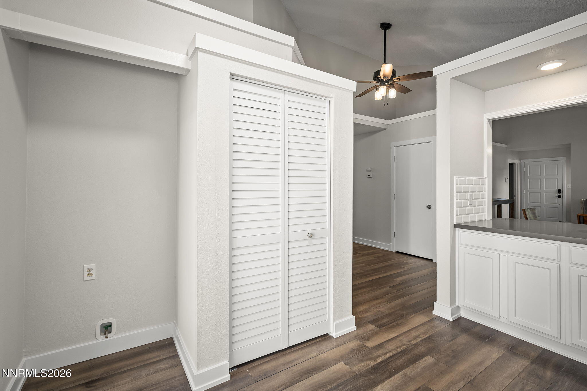 Kitchen and entryway with white louvered closet doors, white cabinetry, and dark wood-look flooring.