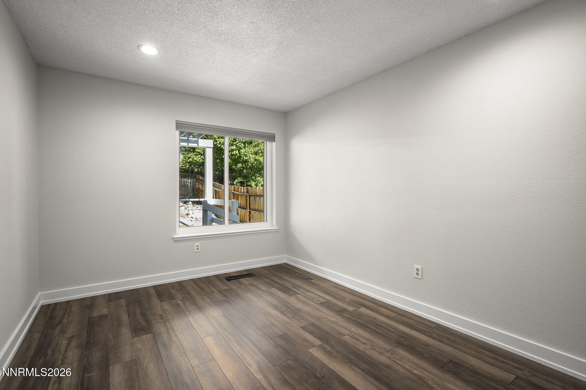 Empty room with dark plank flooring and a window overlooking a fenced yard.
