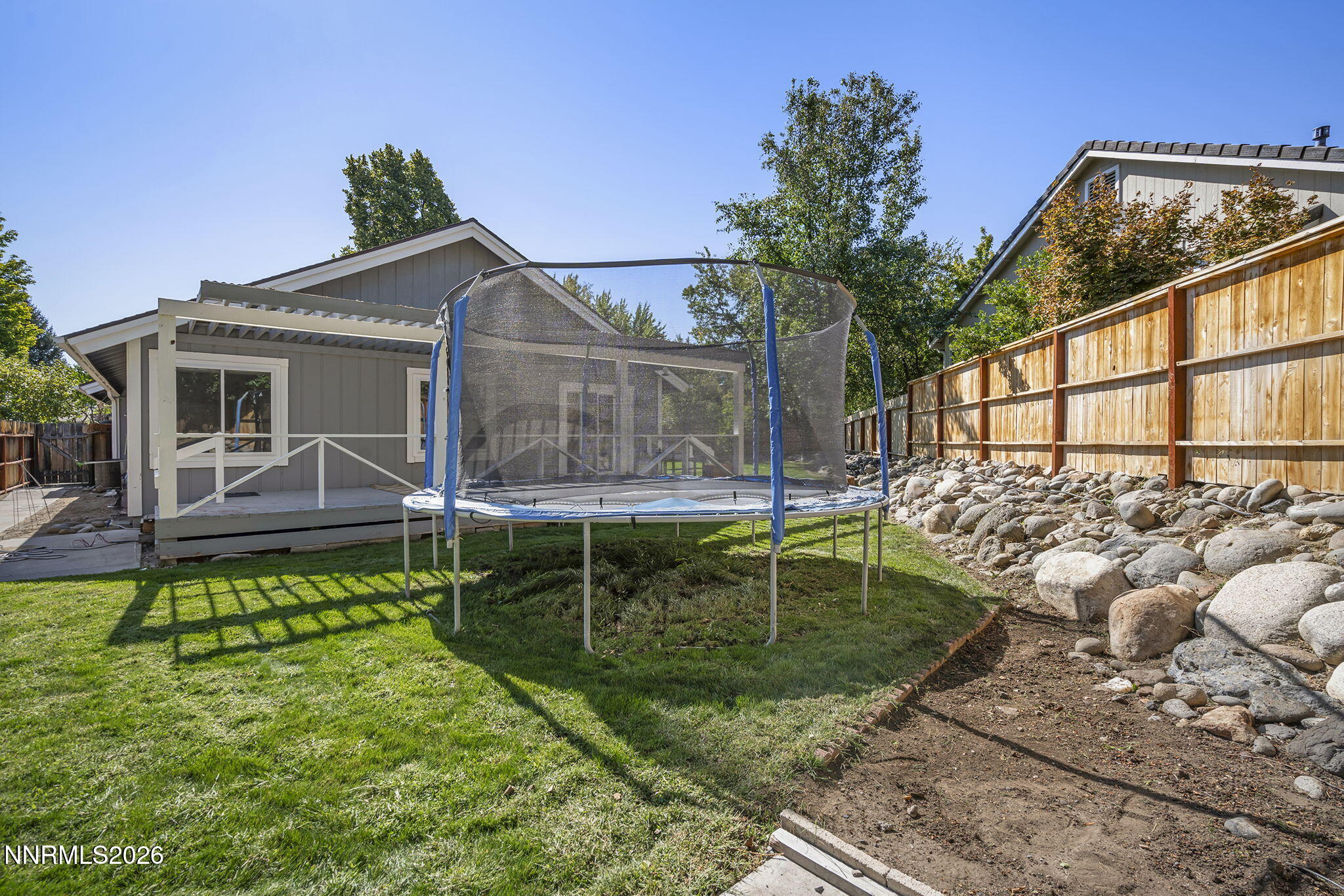 Backyard with a trampoline on the lawn beside a gray home and covered porch.
