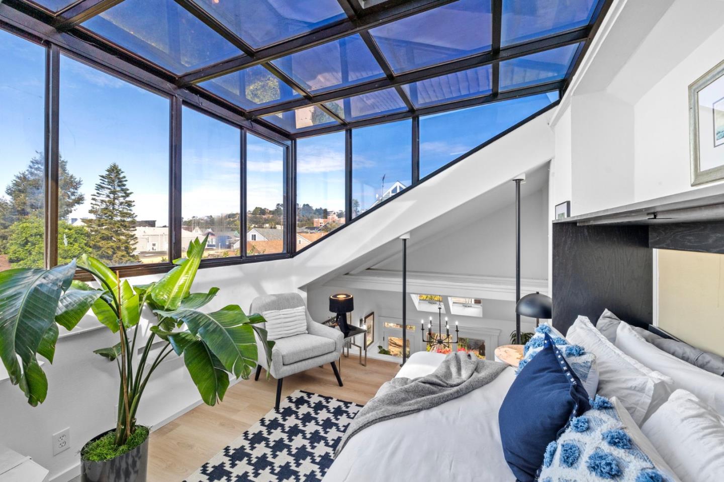 Loft living area with a glass roof, floor-to-ceiling windows, white sofa, and potted plant.