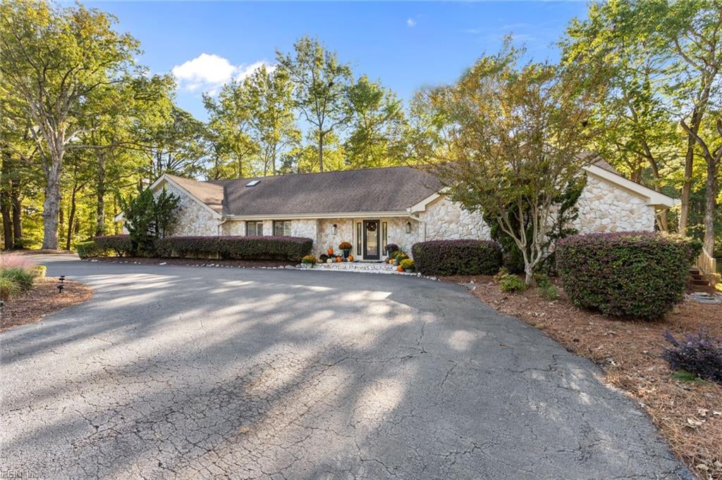 Single-story stone home with a broad curved driveway, mature trees, and autumn decorations by the entrance.