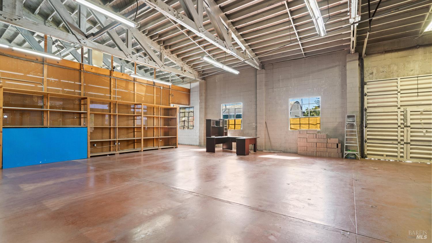 Industrial interior with exposed roof trusses, metal shelving, and a large roll-up garage door.
