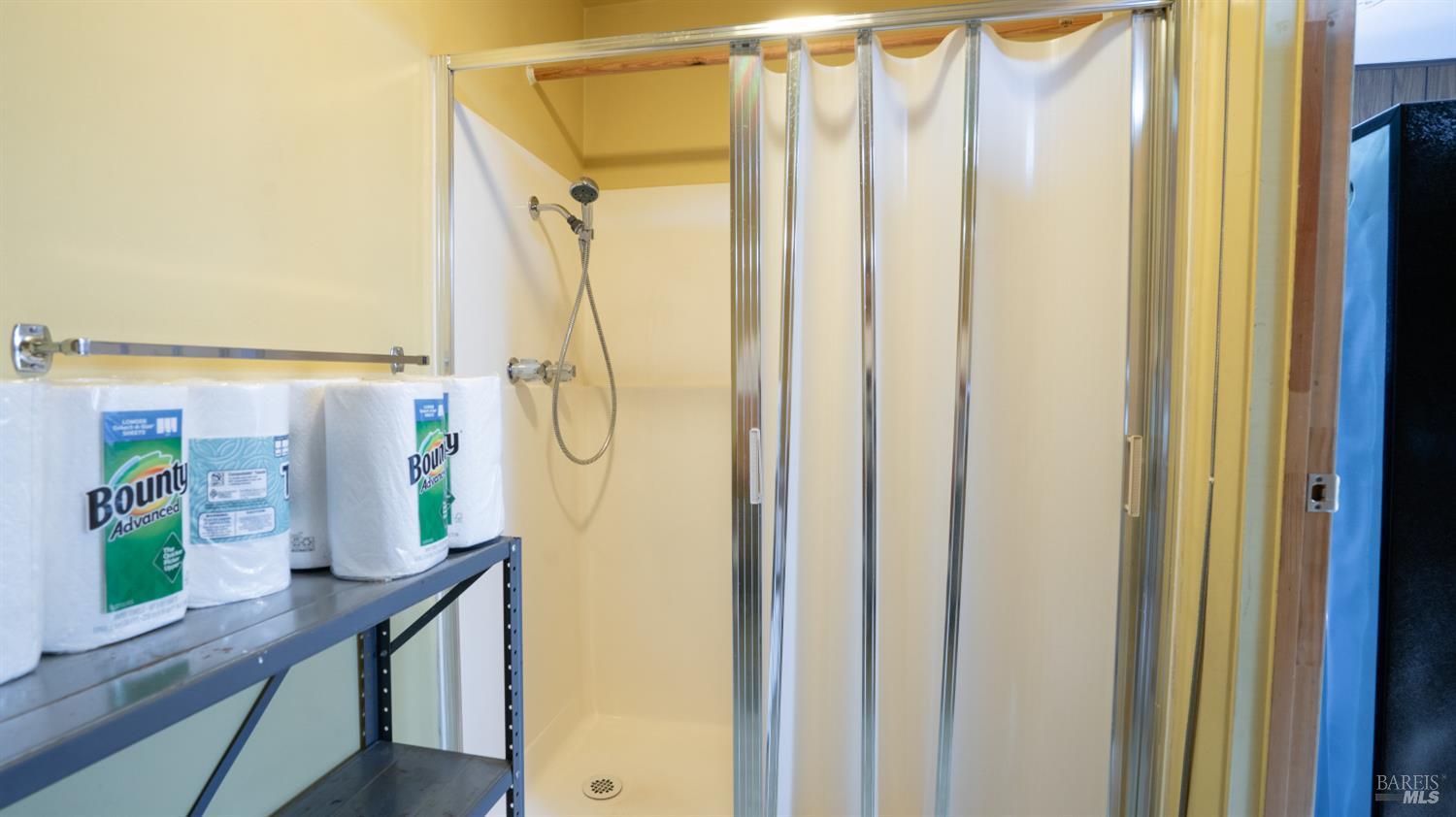 Shower stall with chrome-framed sliding doors and a metal shelf stocked with paper towels.