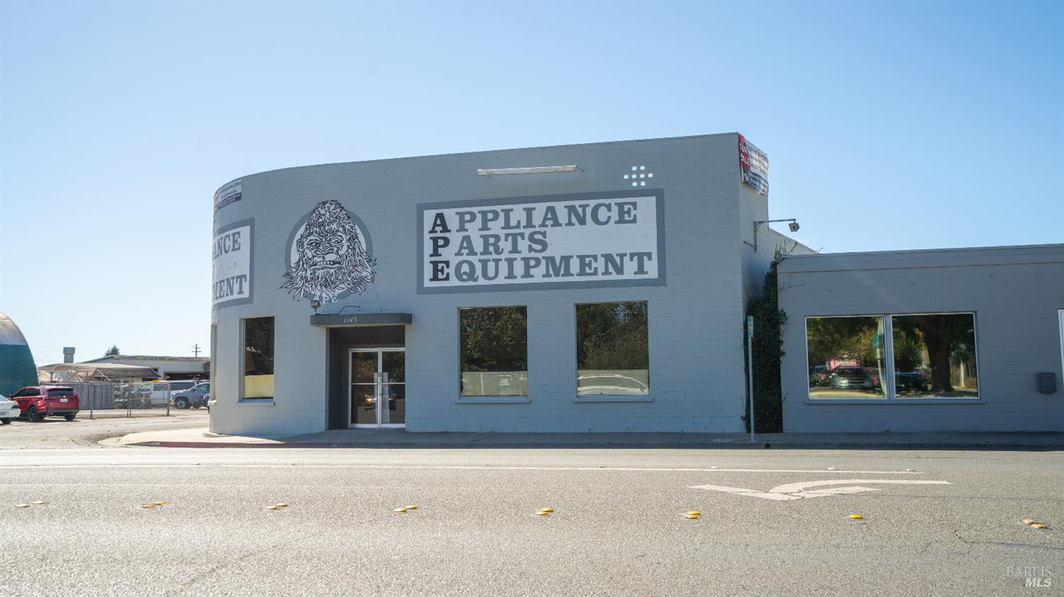 Gray commercial building with an Appliance Parts Equipment sign and illustrated face logo above the entrance.