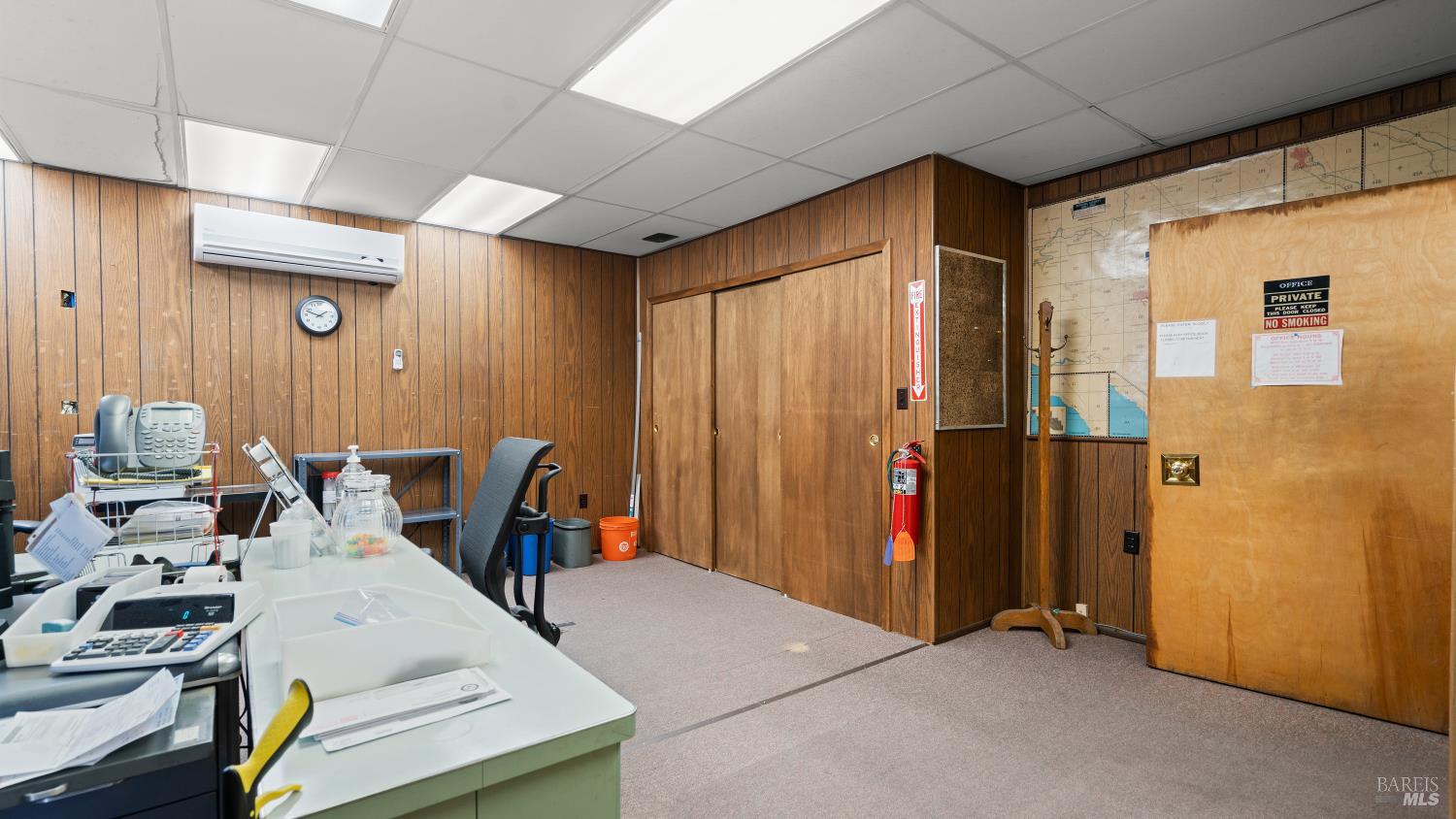 Office with wood-paneled walls, a desk of office equipment, and a large wall map.