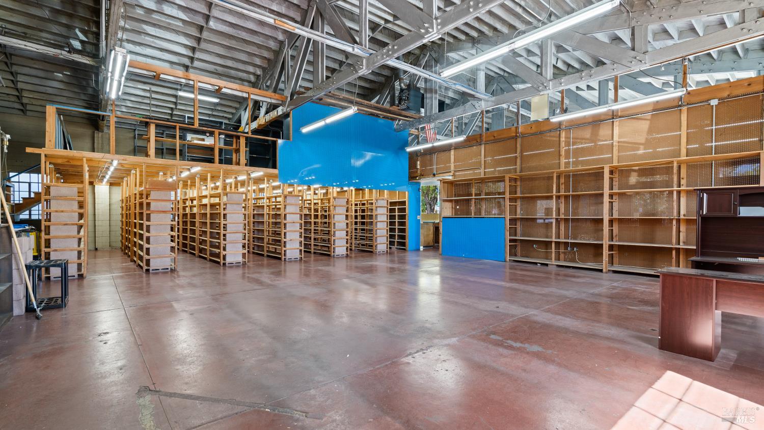 Large commercial interior with rows of wooden shelving, exposed roof trusses, and a blue partition.