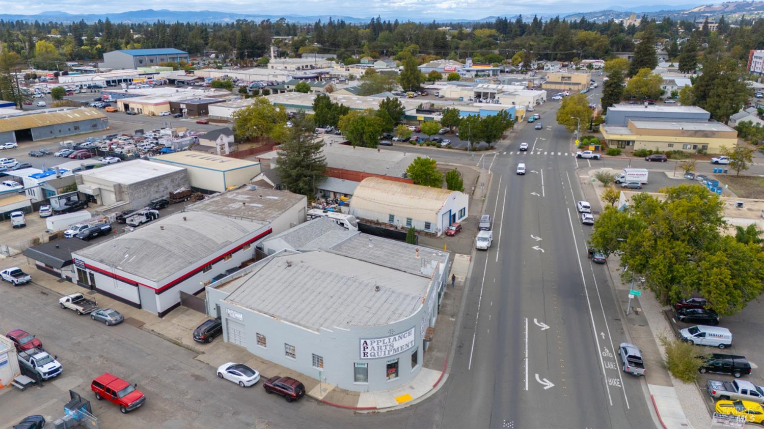 Aerial view of commercial buildings along a broad road, with distant green hills.