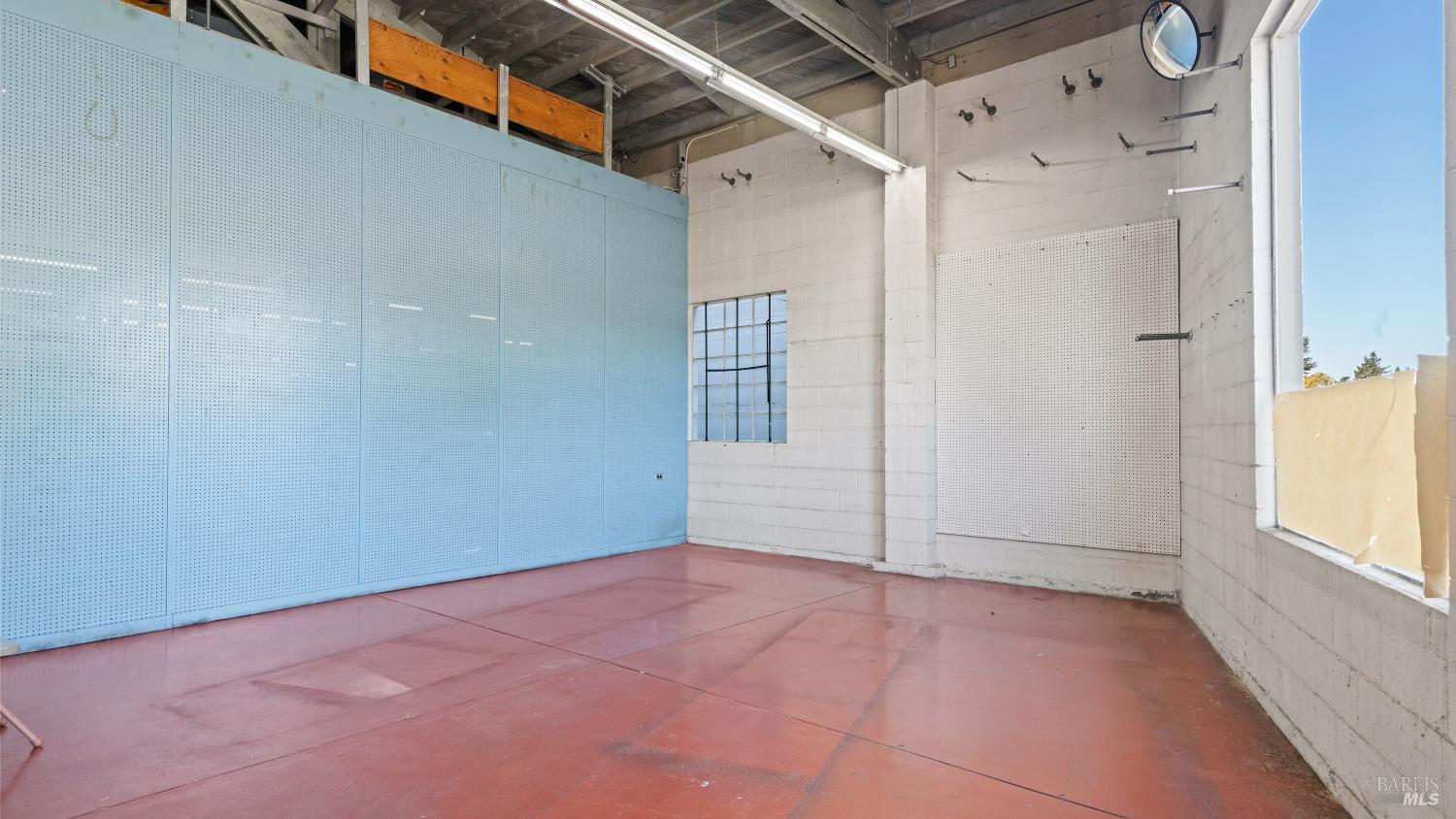 Industrial interior with a red concrete floor, exposed ceiling framing, and large perforated wall panels.