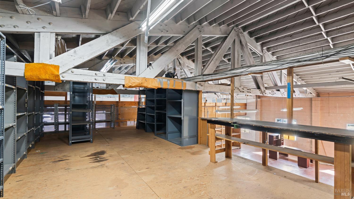 Unfinished interior with exposed timber trusses, metal shelving, and a raised storage platform.