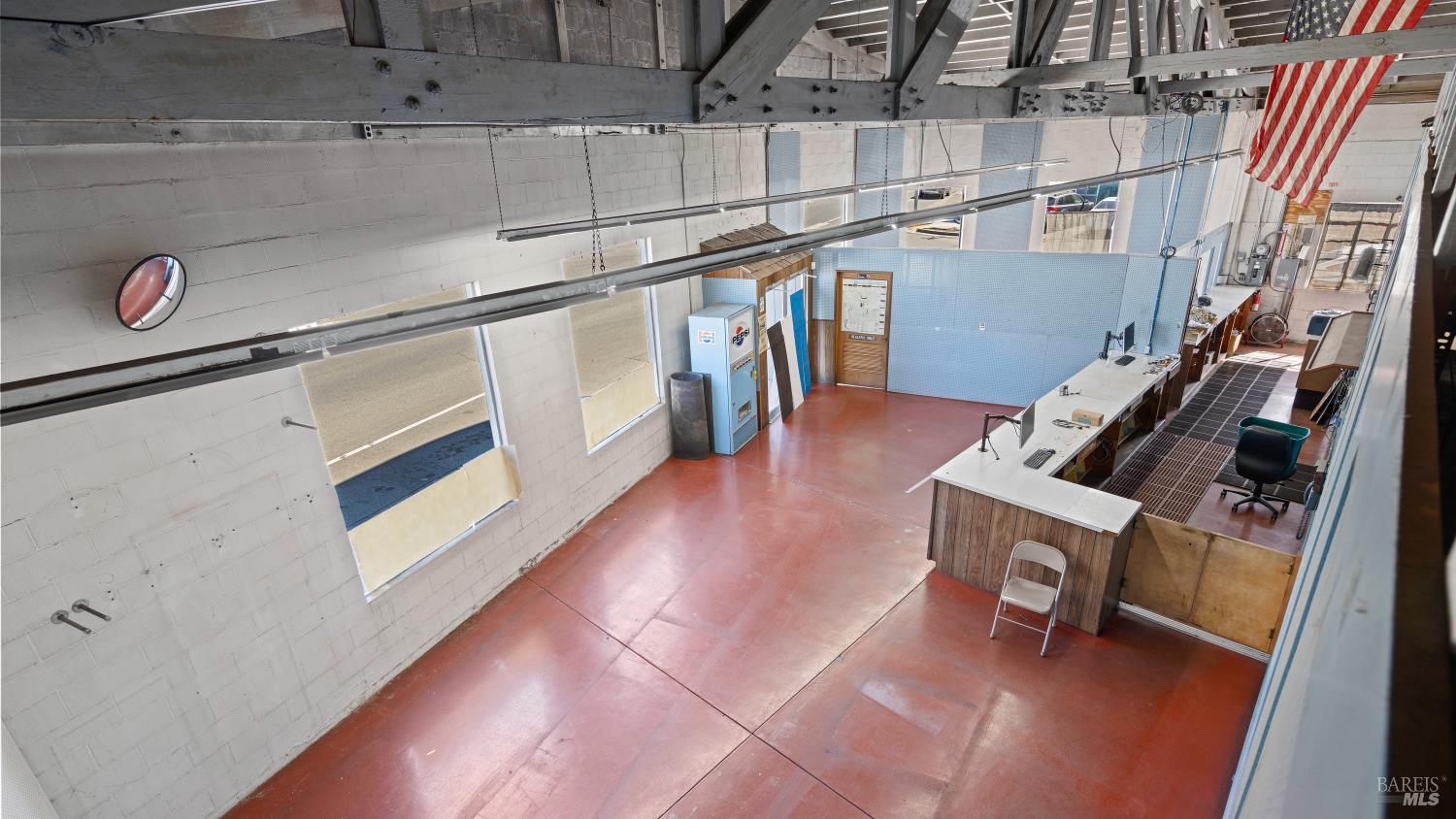 Vacant garage interior with red concrete floor, long service counter, exposed trusses, and American flag.