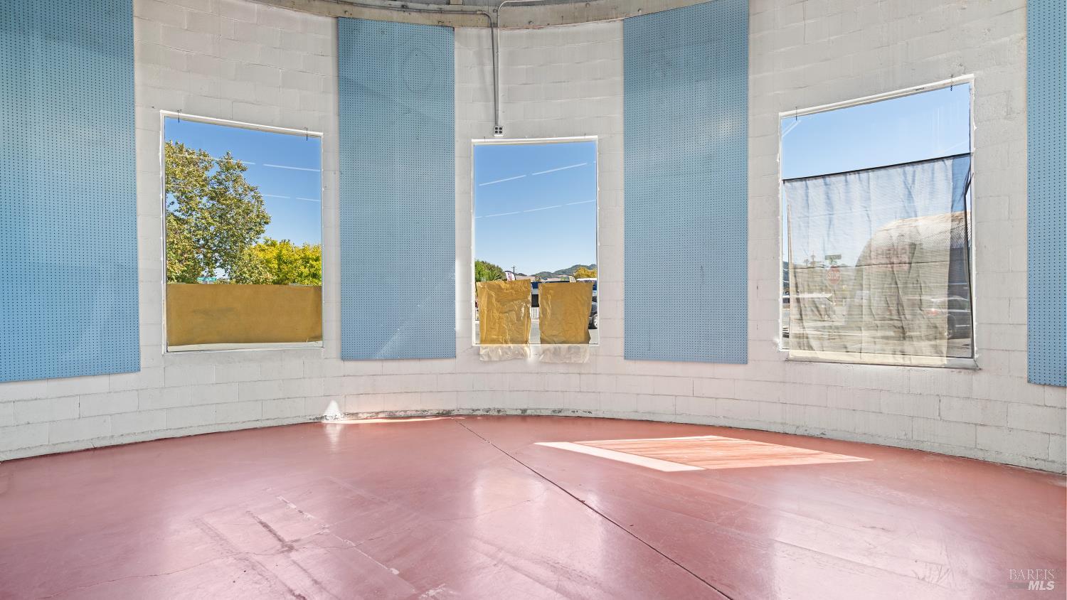 Empty curved room with blue acoustic panels, a pink floor, and tall windows.