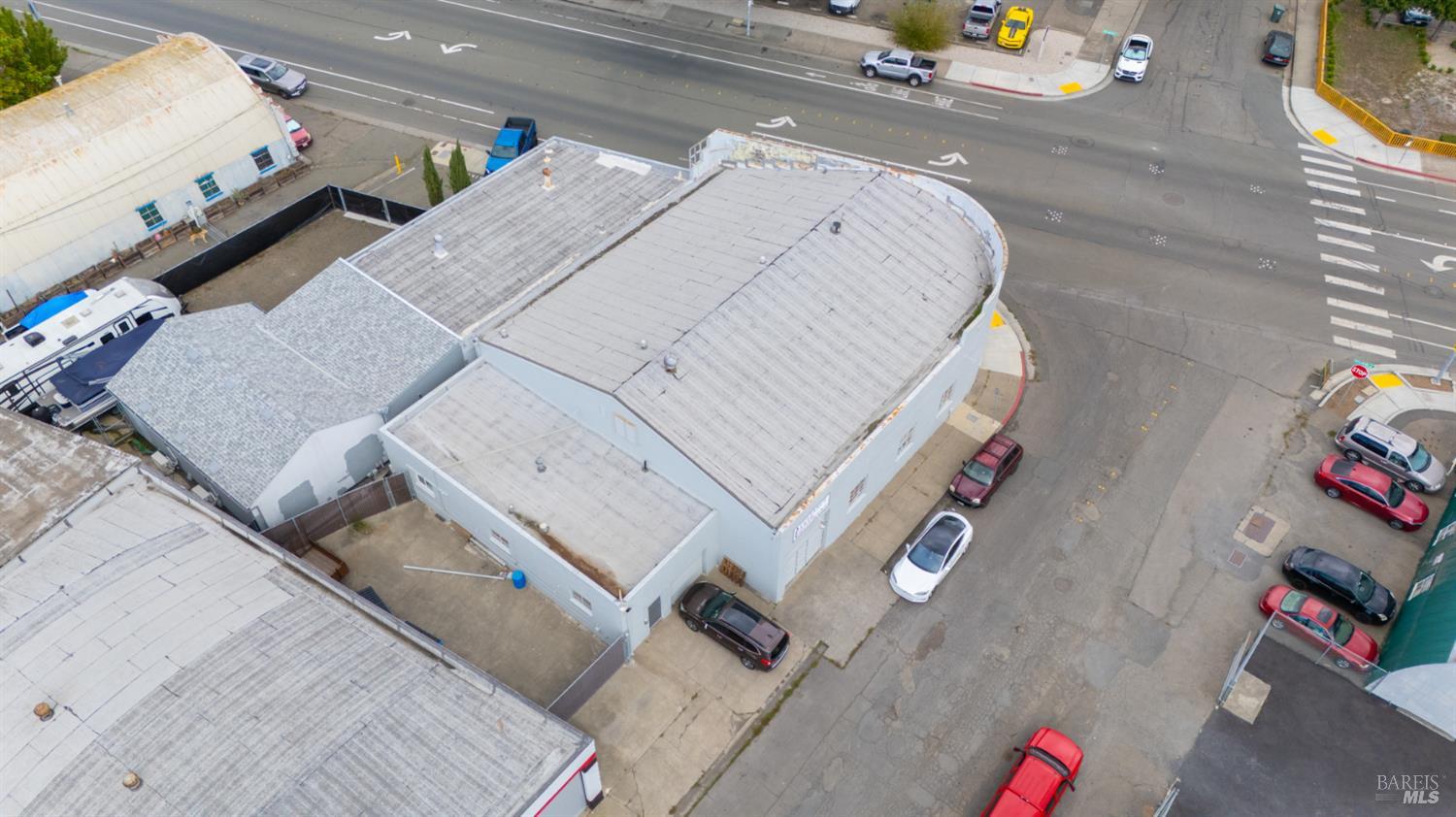 Aerial view of a flat-roofed commercial building at a street corner, with surrounding roads and parked cars.