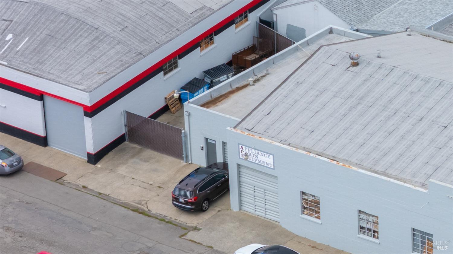 Aerial view of gray commercial buildings with red trim, loading areas, and parked cars.