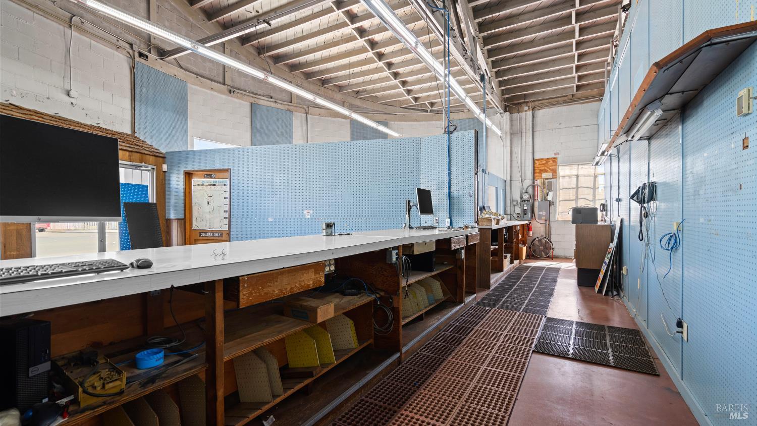 Commercial workshop with a long work counter, blue pegboard walls, and grated floor mats.