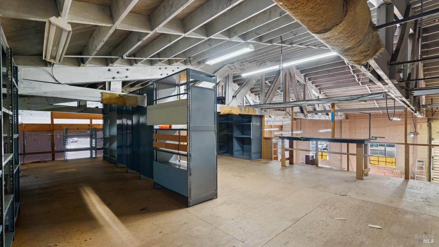 Unfinished industrial interior with exposed roof trusses and metal shelving on a plywood mezzanine.