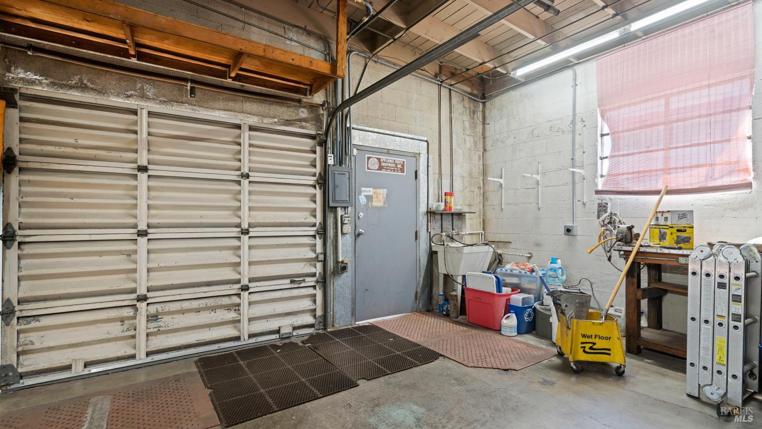 Garage workshop with a wide sectional door, utility sink, cleaning equipment, and exposed ceiling beams.