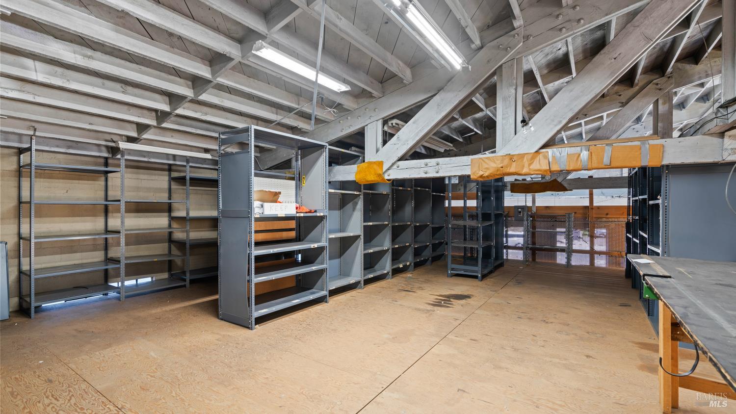 Commercial storage space with metal shelving, workbenches, and exposed roof trusses.