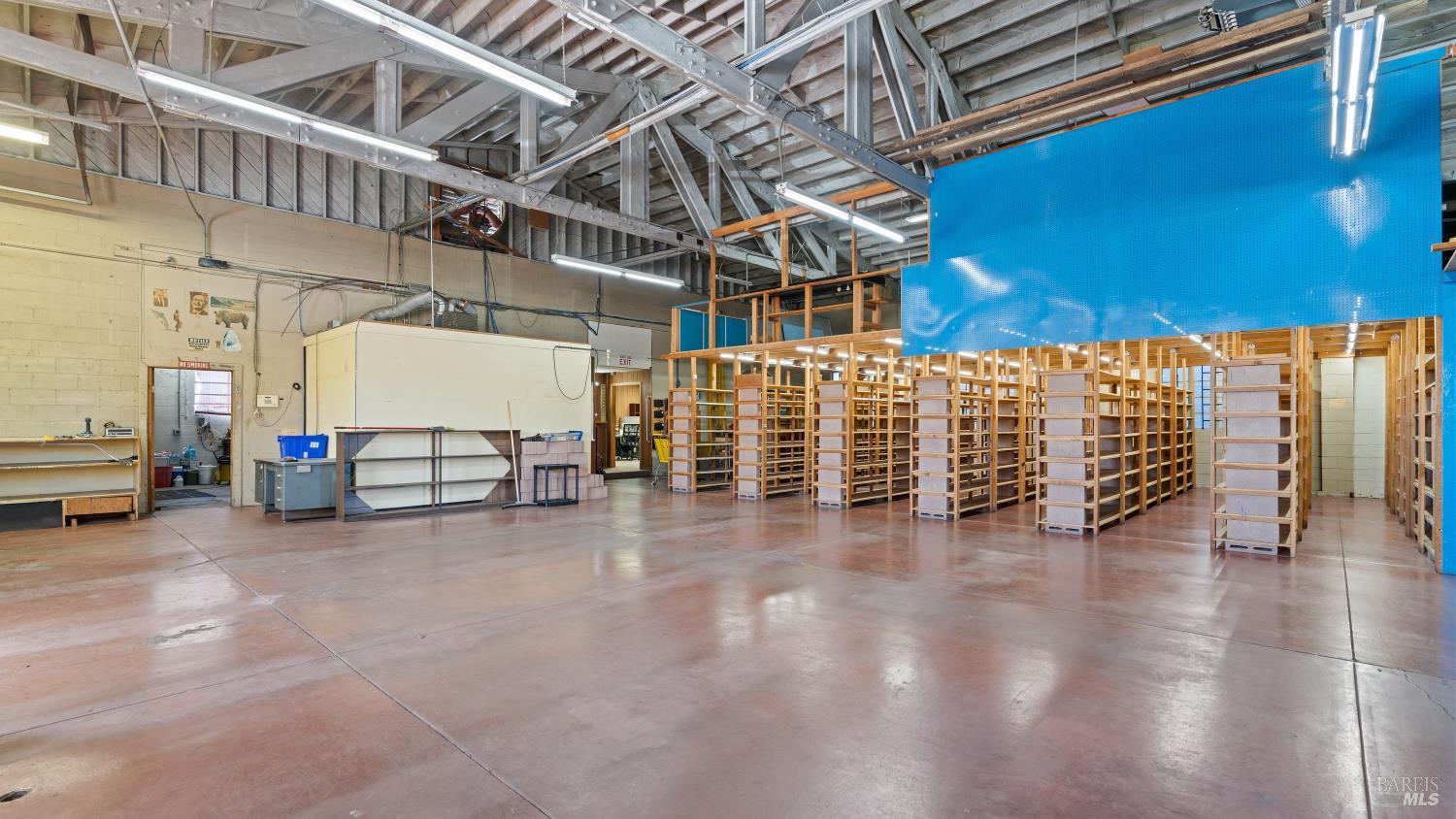 Large commercial interior with rows of wooden shelving, exposed roof trusses, and a blue partition wall.