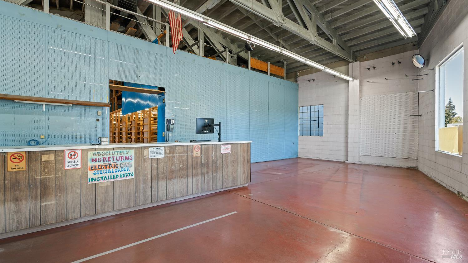 Commercial workshop interior with a long service counter, blue wall panels, exposed rafters, and red concrete floor.