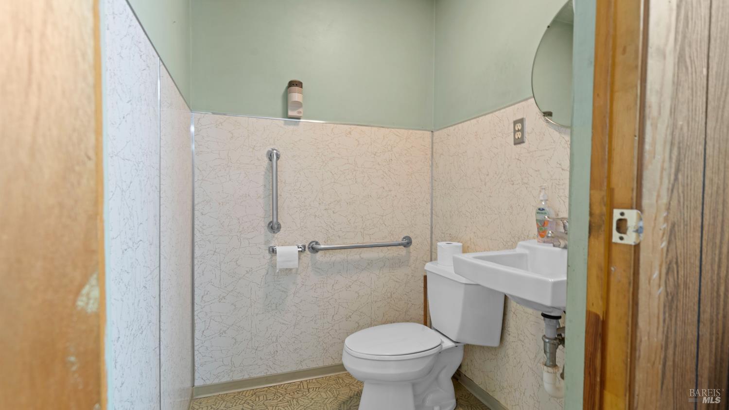 Bathroom with a toilet, wall-mounted sink, grab bars, and patterned wall and floor finishes.