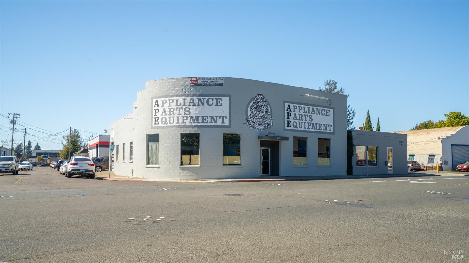 Gray commercial building with two Appliance Parts Equipment signs and an illustrated face on its facade.
