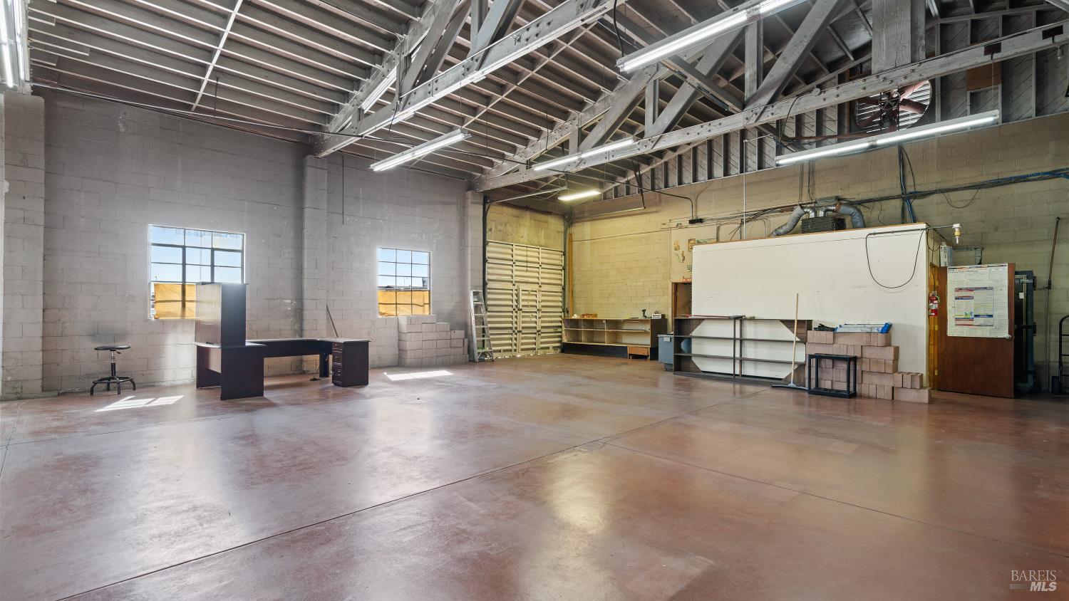 Industrial workshop with exposed roof trusses, high windows, and shelving along the walls.