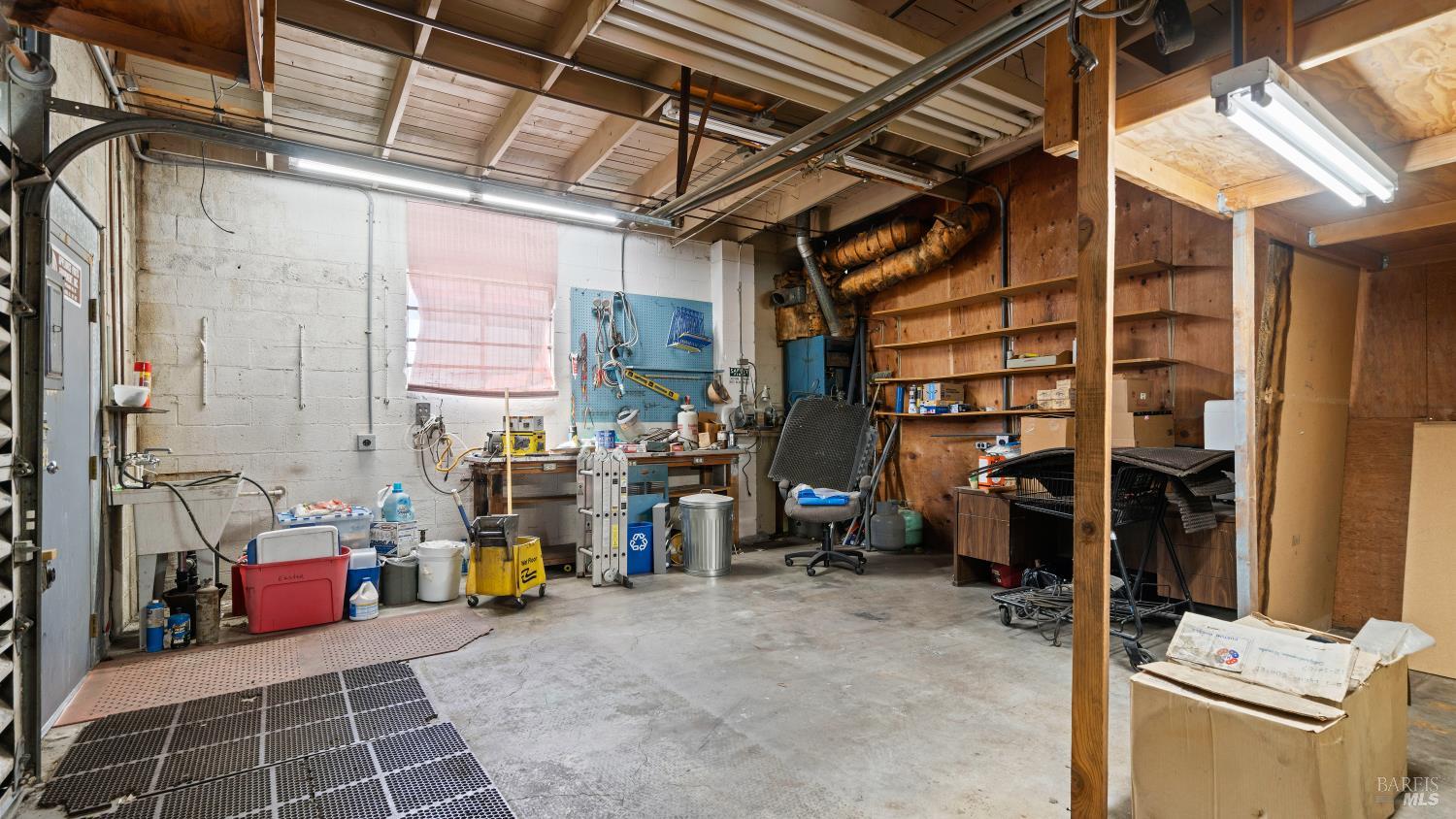 Garage workshop with exposed beams, wooden shelving, workbenches, and tools.