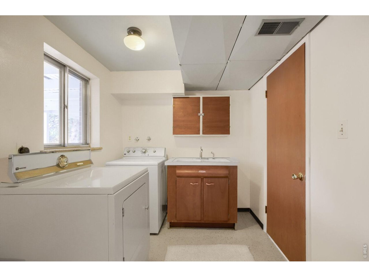 Laundry room with Maytag washer, utility sink, wood cabinets, and a window.
