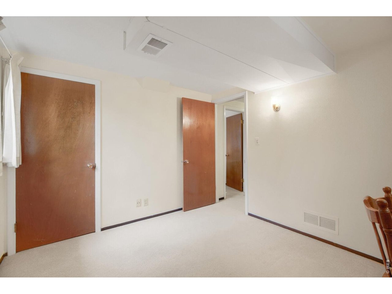 Carpeted room with cream walls, multiple wooden doors, and a ceiling vent.