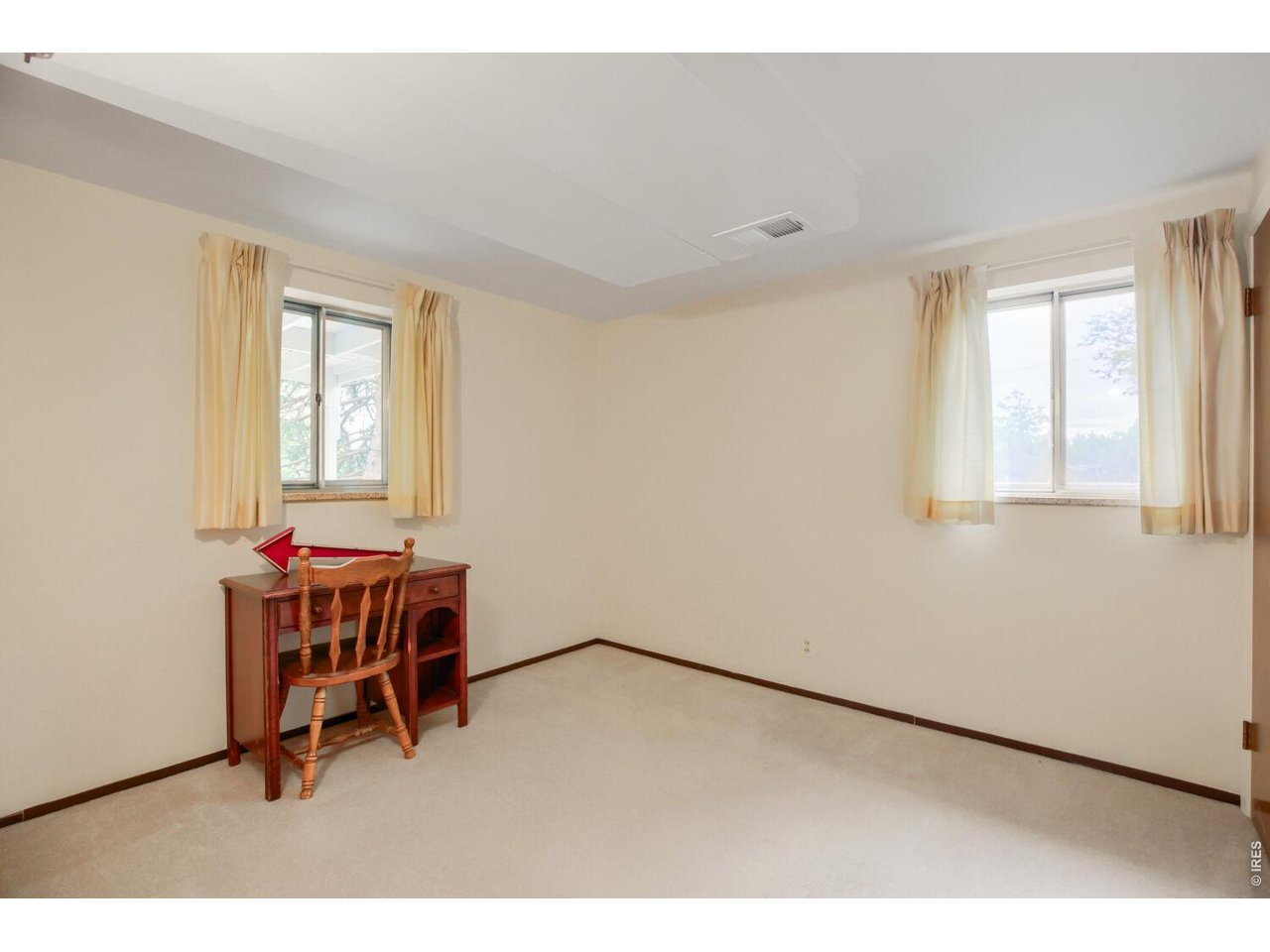 Sparsely furnished room with two curtained windows and a wooden desk and chair.