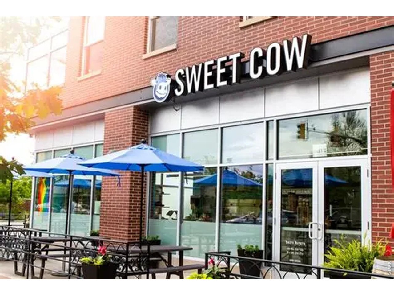 Sweet Cow storefront with a brick facade and patio tables shaded by blue umbrellas.