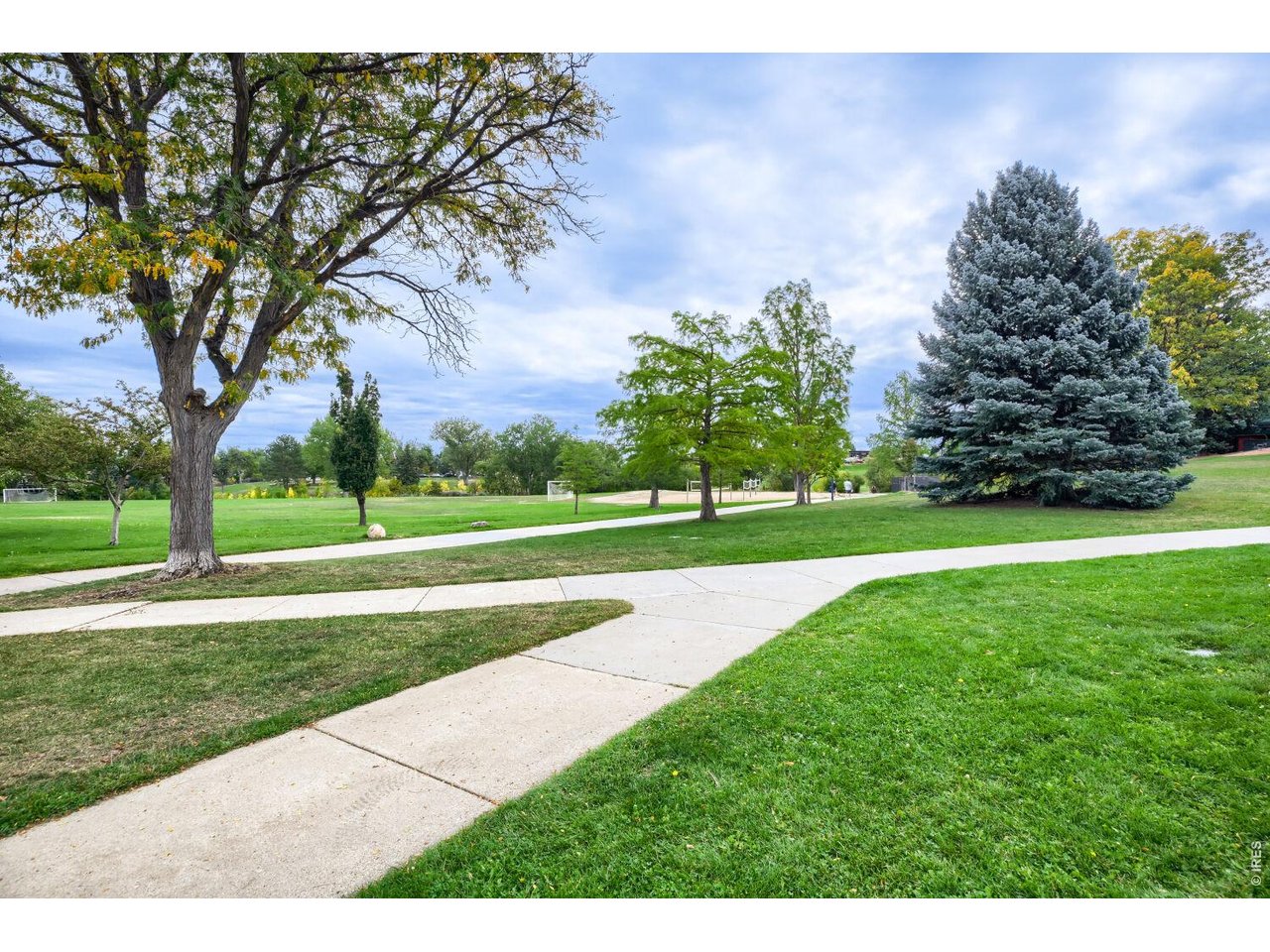 Green park with mature trees, broad lawns, and intersecting paved paths.