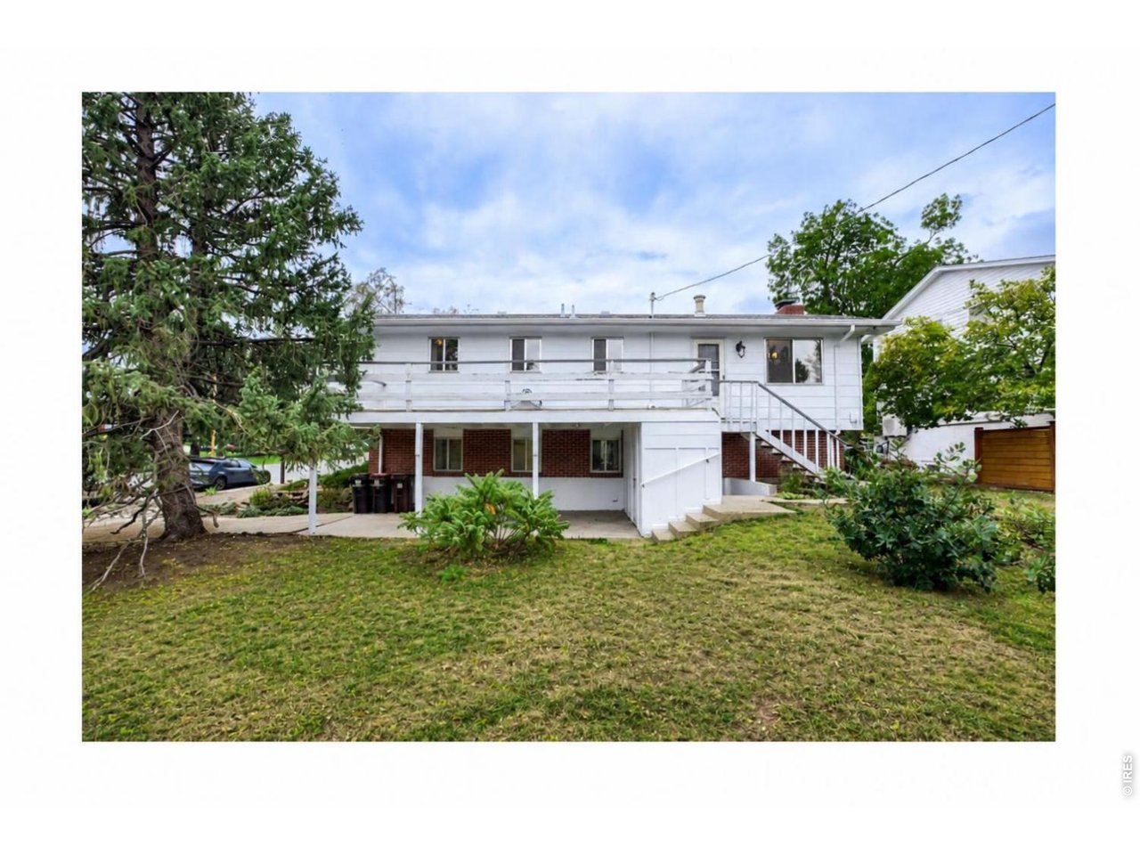 Rear of a white split-level house with an elevated deck and exterior stairs overlooking a grassy yard.
