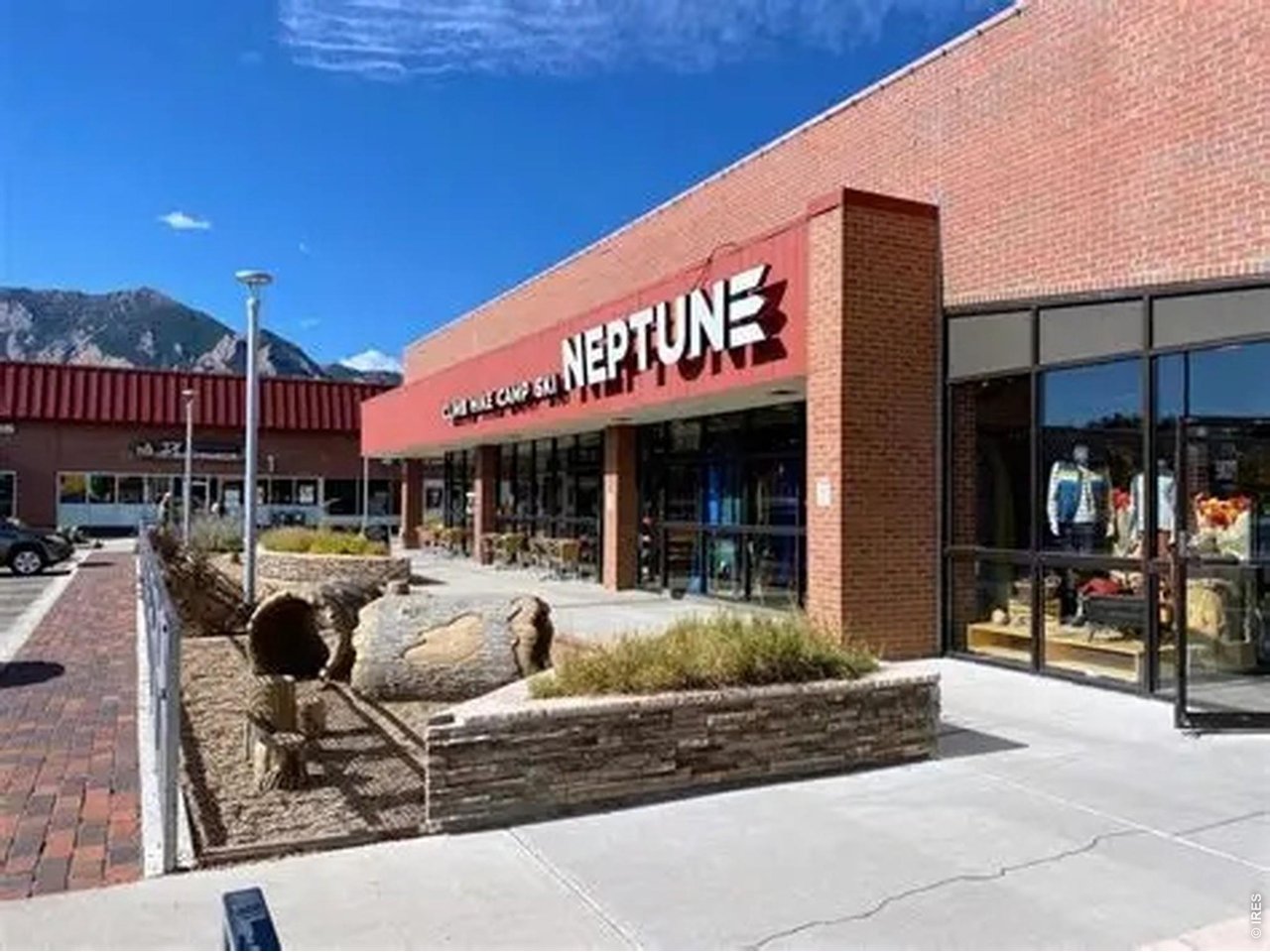 Brick Neptune storefront with glass windows, a stone planter, and mountains in the background.