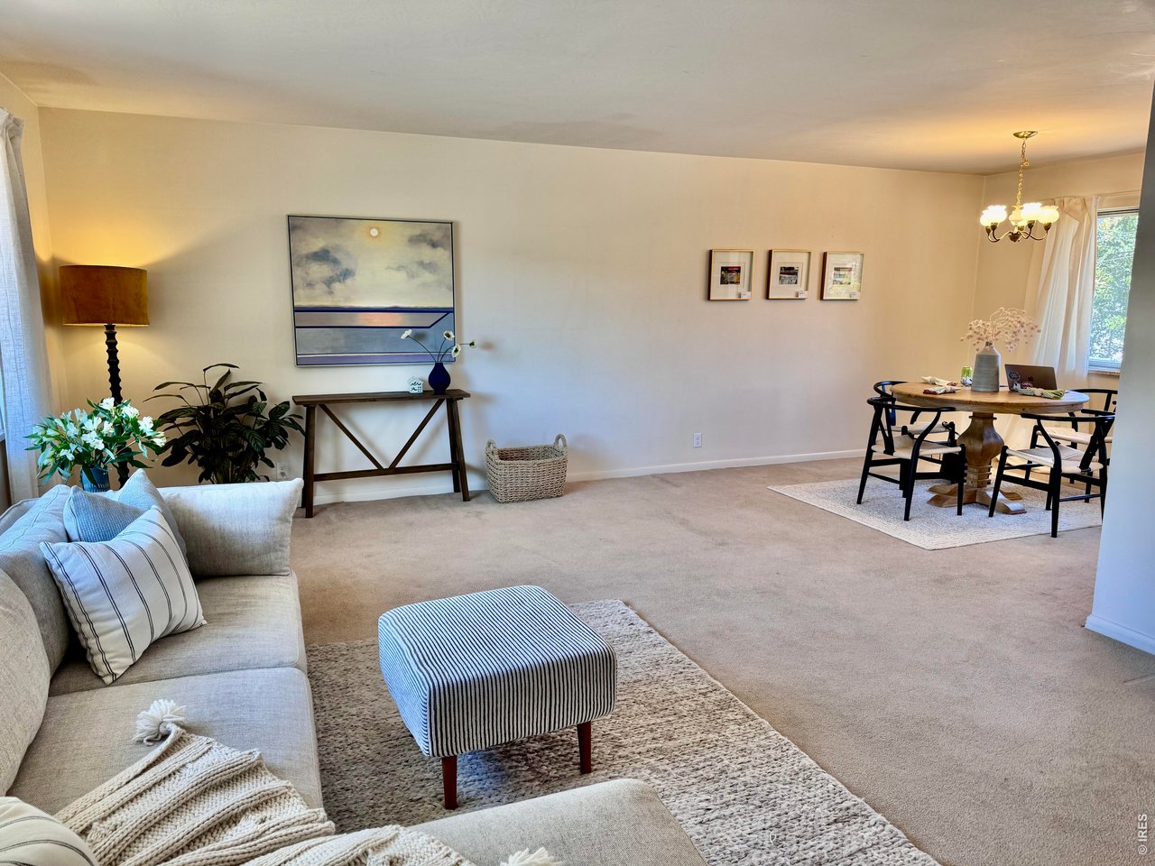 Living room with a striped ottoman, console artwork, and an adjoining dining area by the windows.