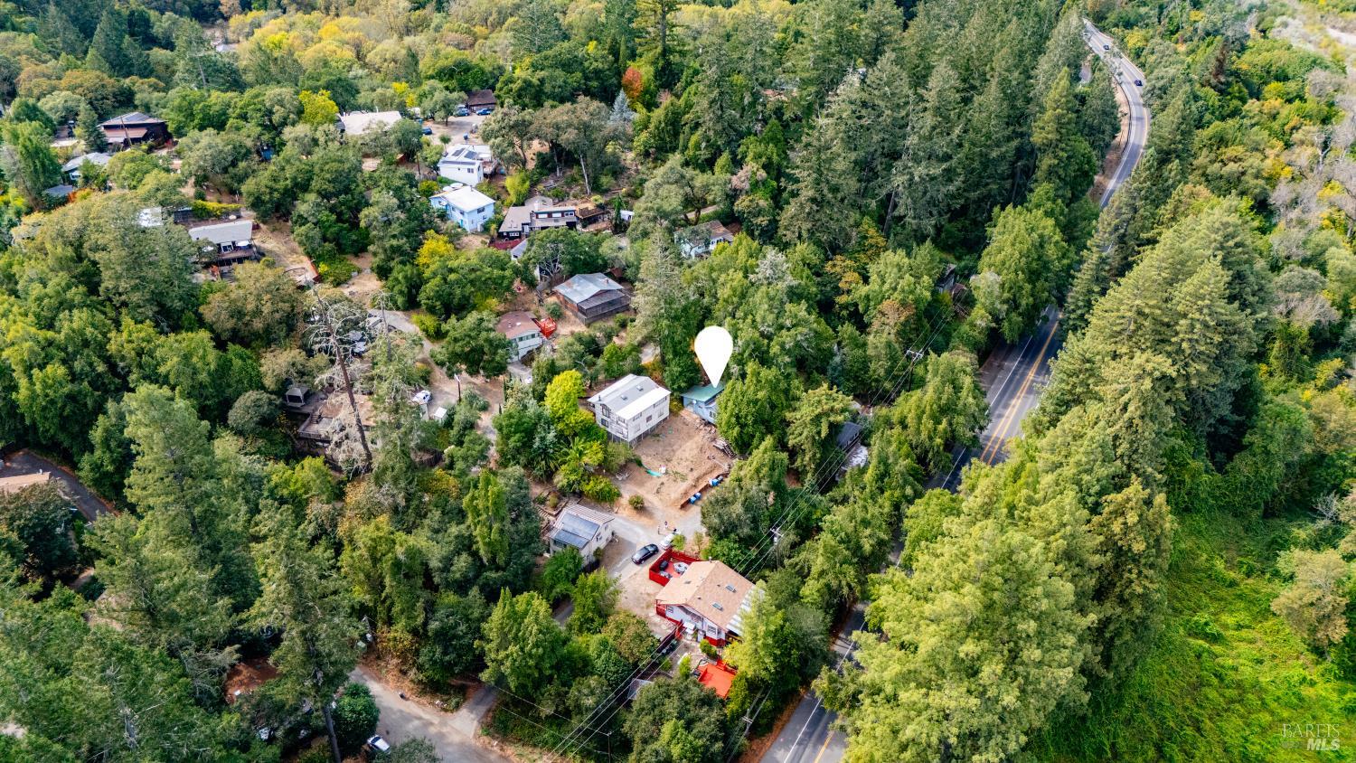 Aerial view of a wooded neighborhood, with a map marker above a house beside a winding road.