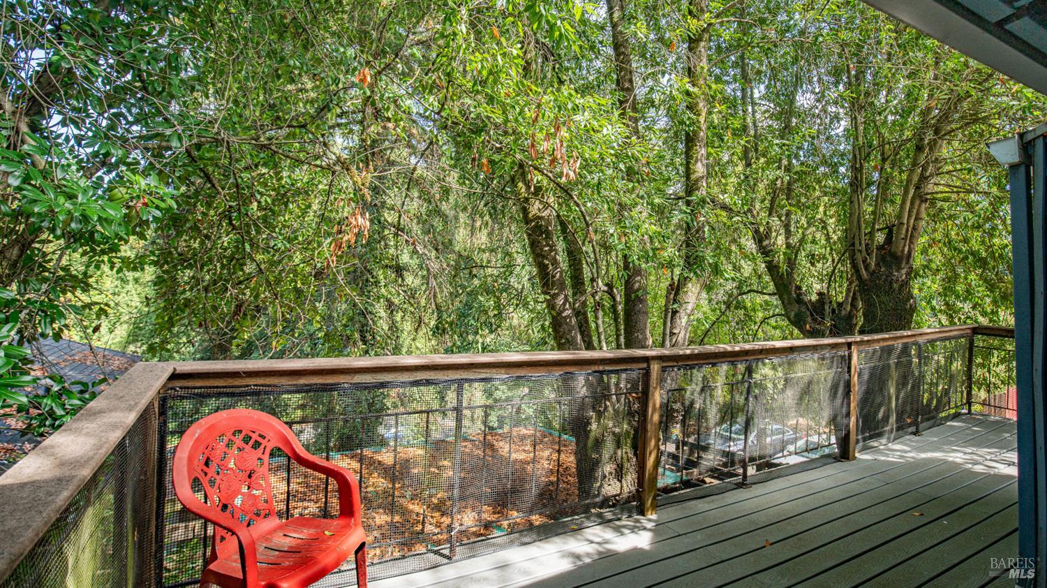 Wooden deck with a red chair overlooking dense trees.