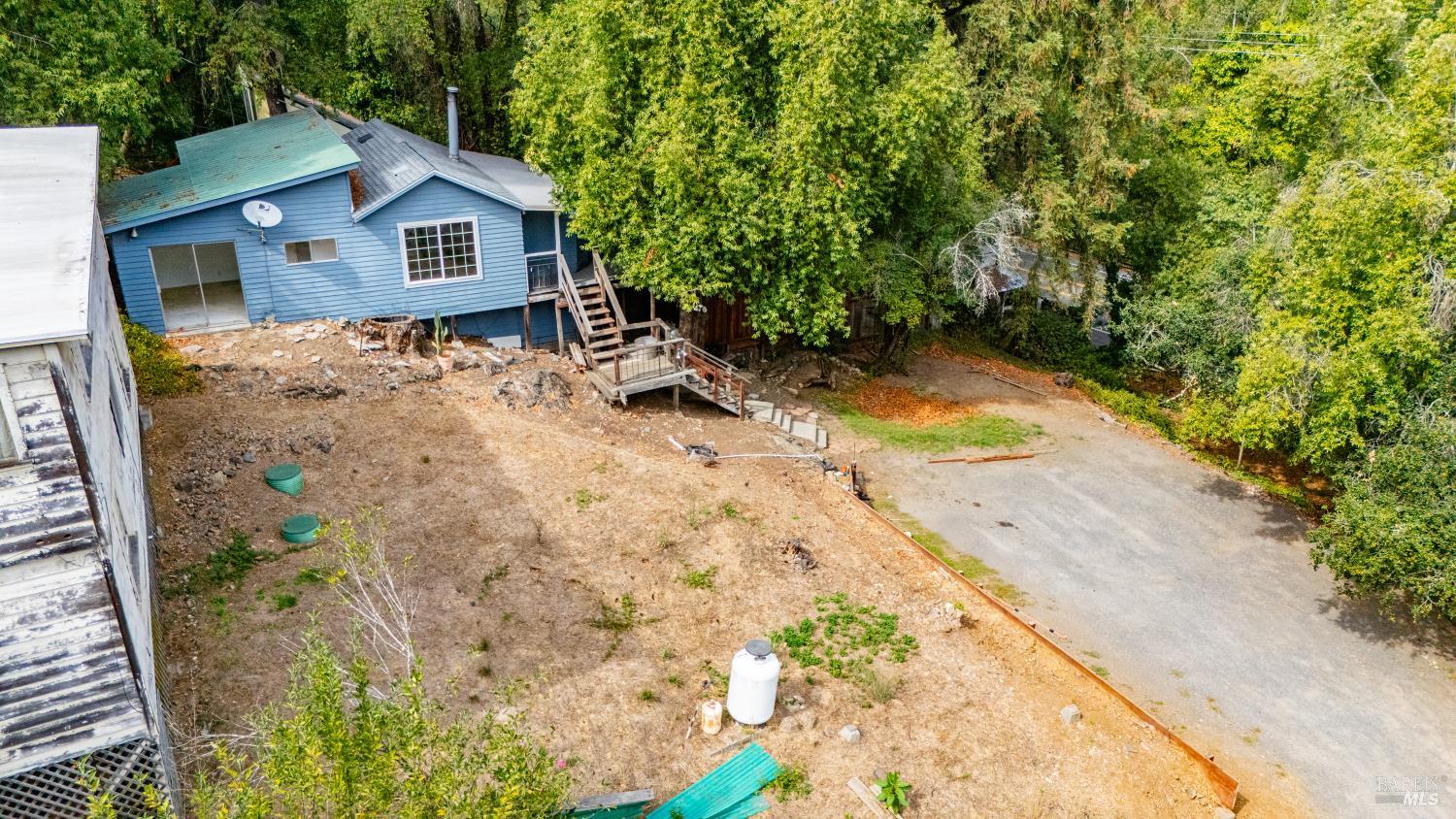 Aerial view of a blue house with a wooden deck, dry yard, and paved driveway.