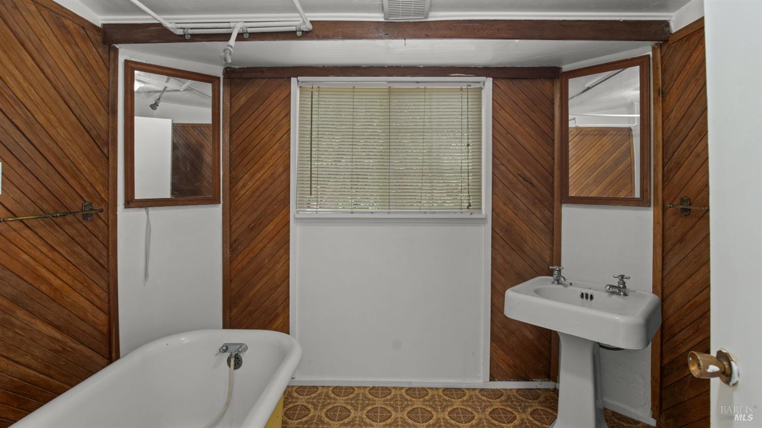 Bathroom with a white bathtub, pedestal sink, and diagonal wood-paneled walls.
