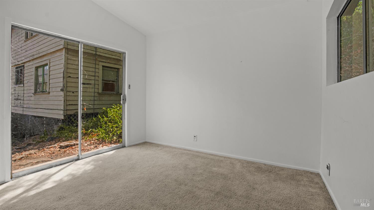 Empty carpeted room with a sliding glass door and sunlight across the floor.