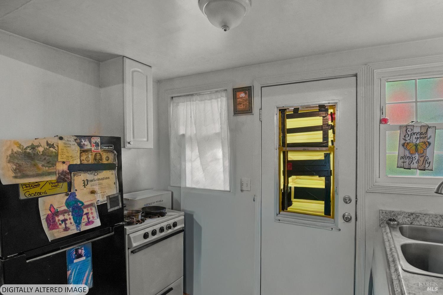 Kitchen with an artwork-covered refrigerator, white stove, double sink, and back door.