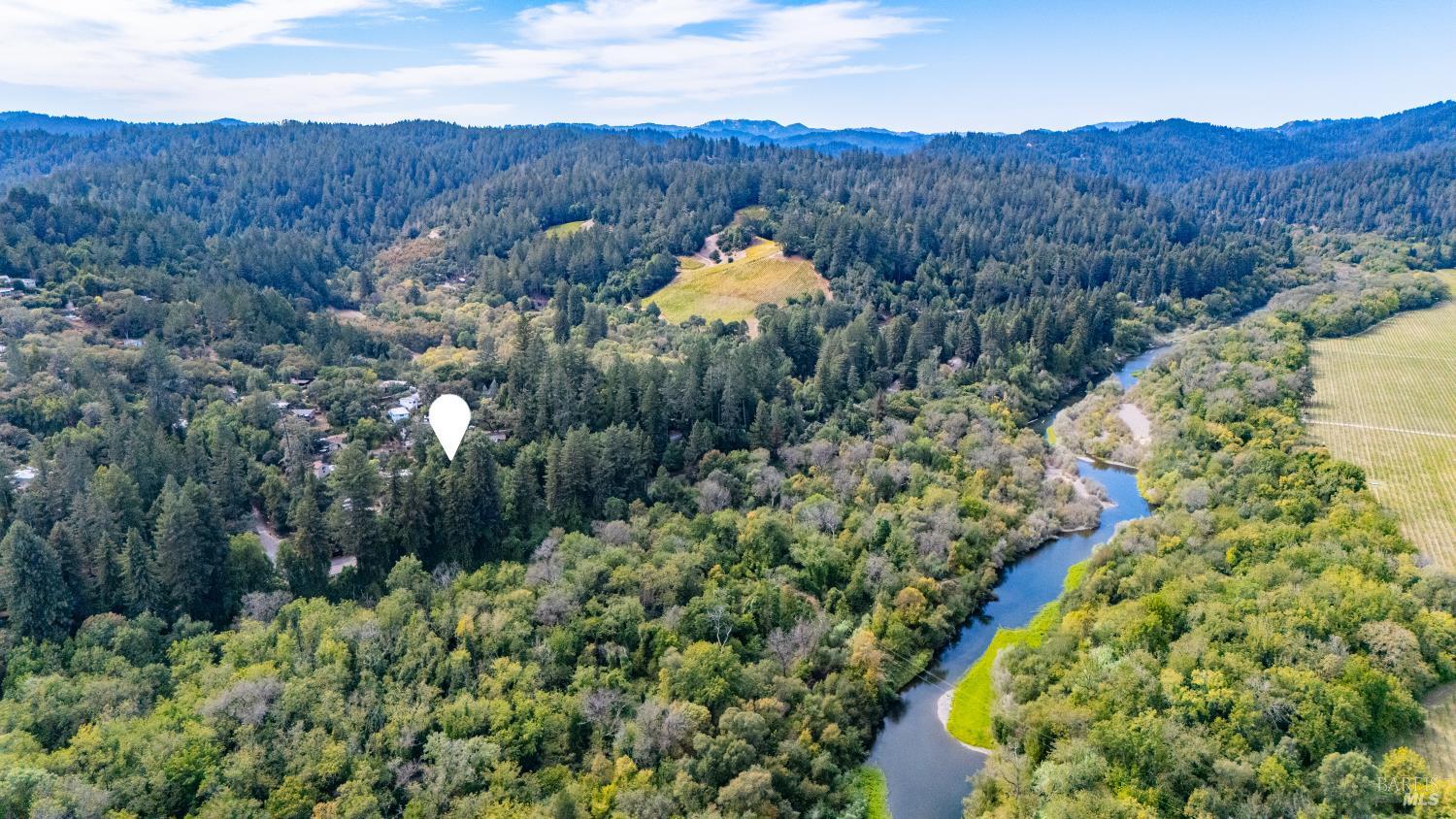 Aerial view of a wooded property marked by a pin, with a winding river and vineyard rows nearby.