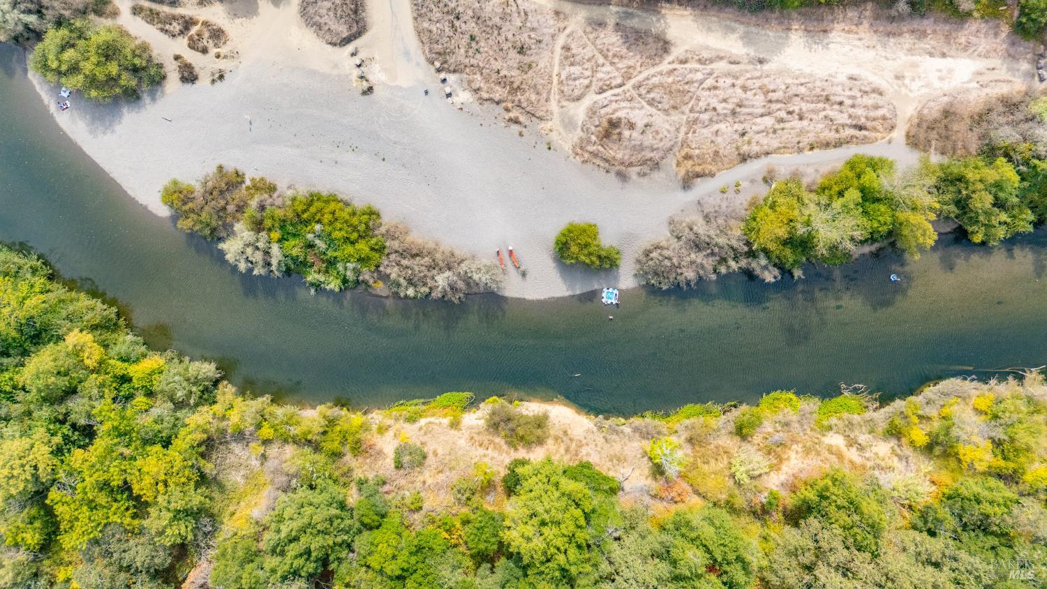 Aerial view of a river bordered by sandy banks, shrubs, and trees.