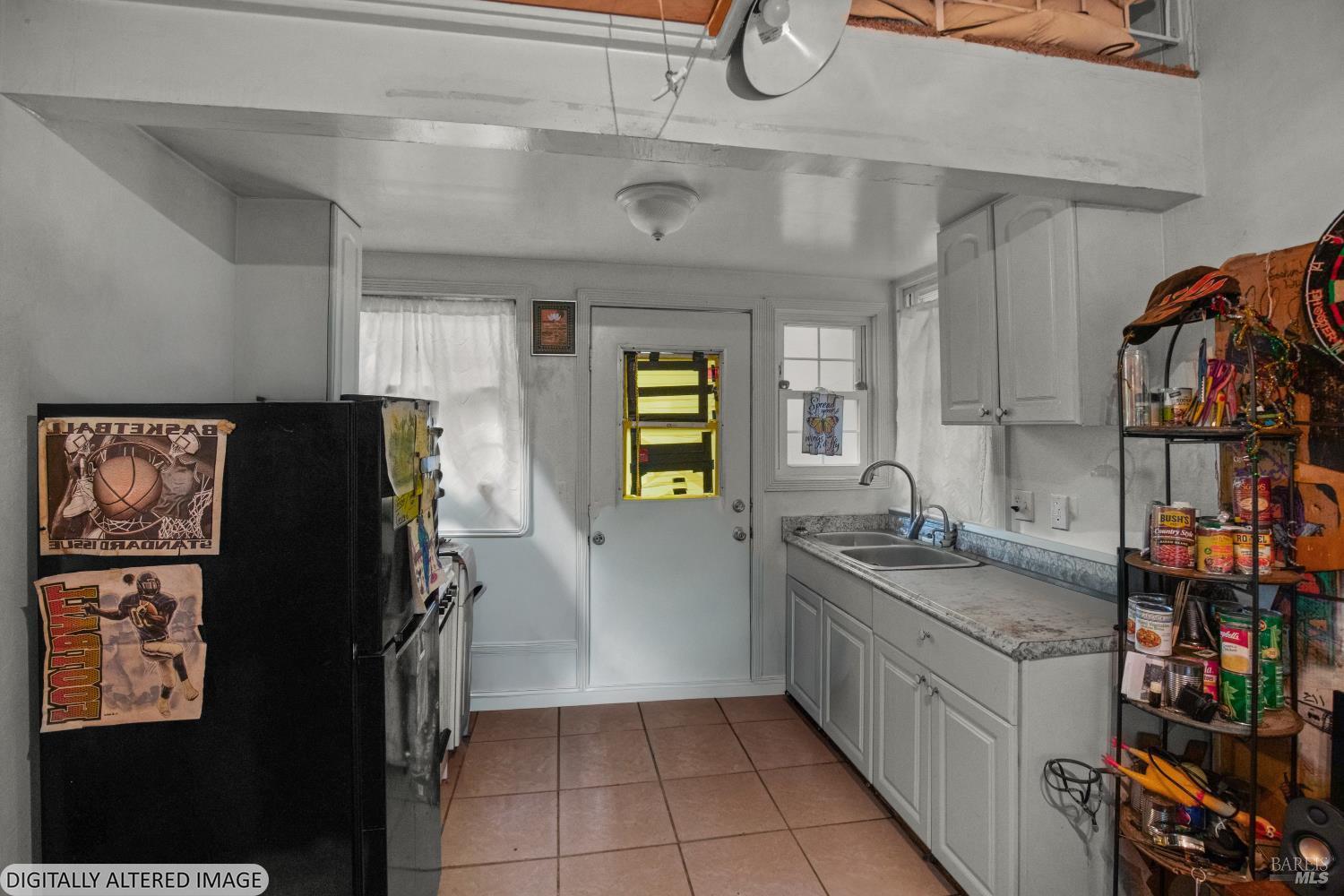 Compact kitchen with gray cabinets, a long sink counter, black refrigerator, and stocked shelving.