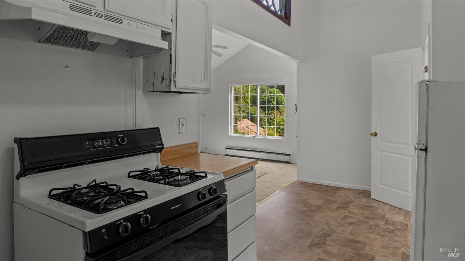Kitchen with a white gas range and wood countertop opening onto a bright adjoining room.