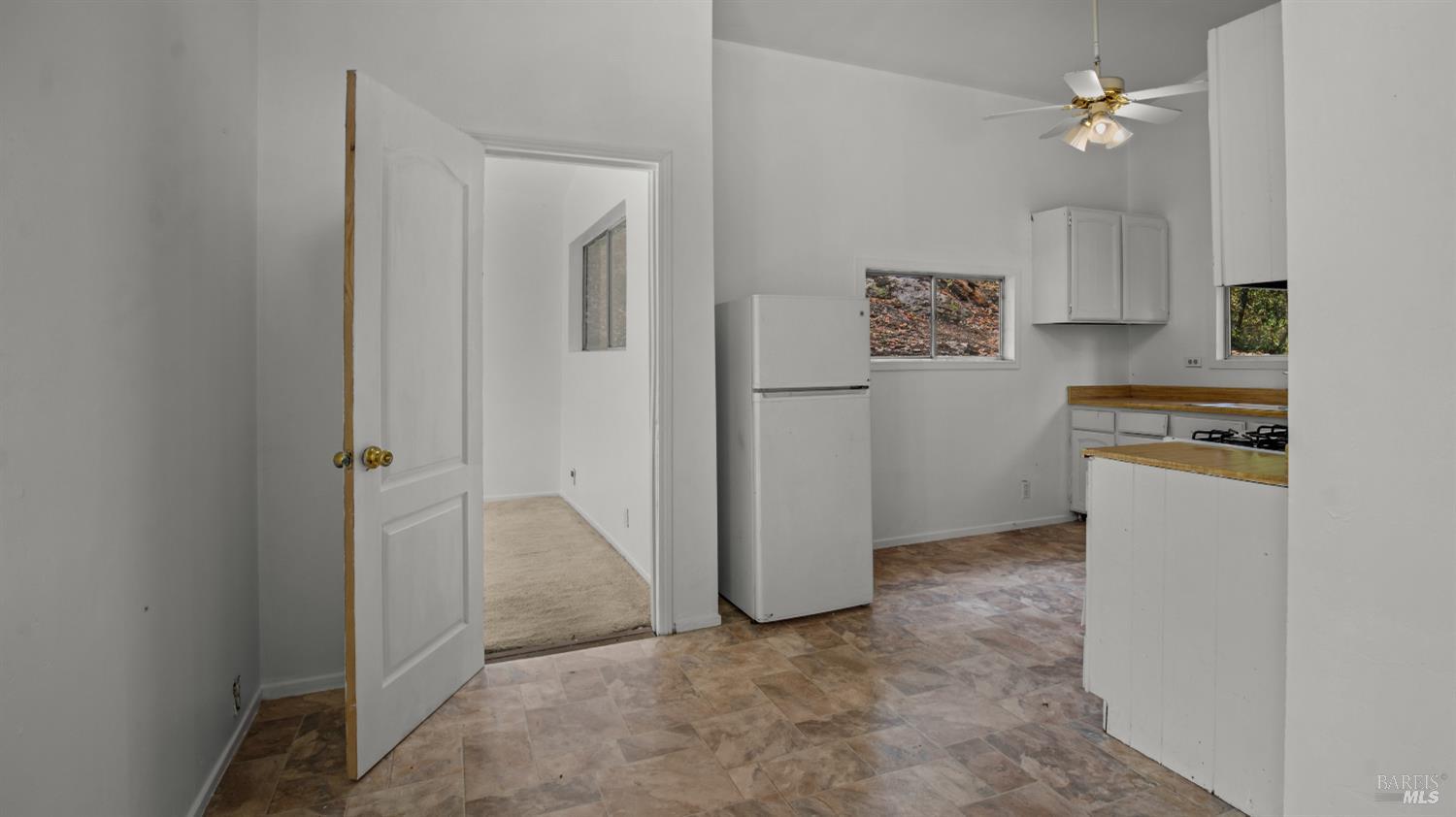 Unfurnished kitchen with white cabinets, wood countertops, and a refrigerator beside an open doorway.