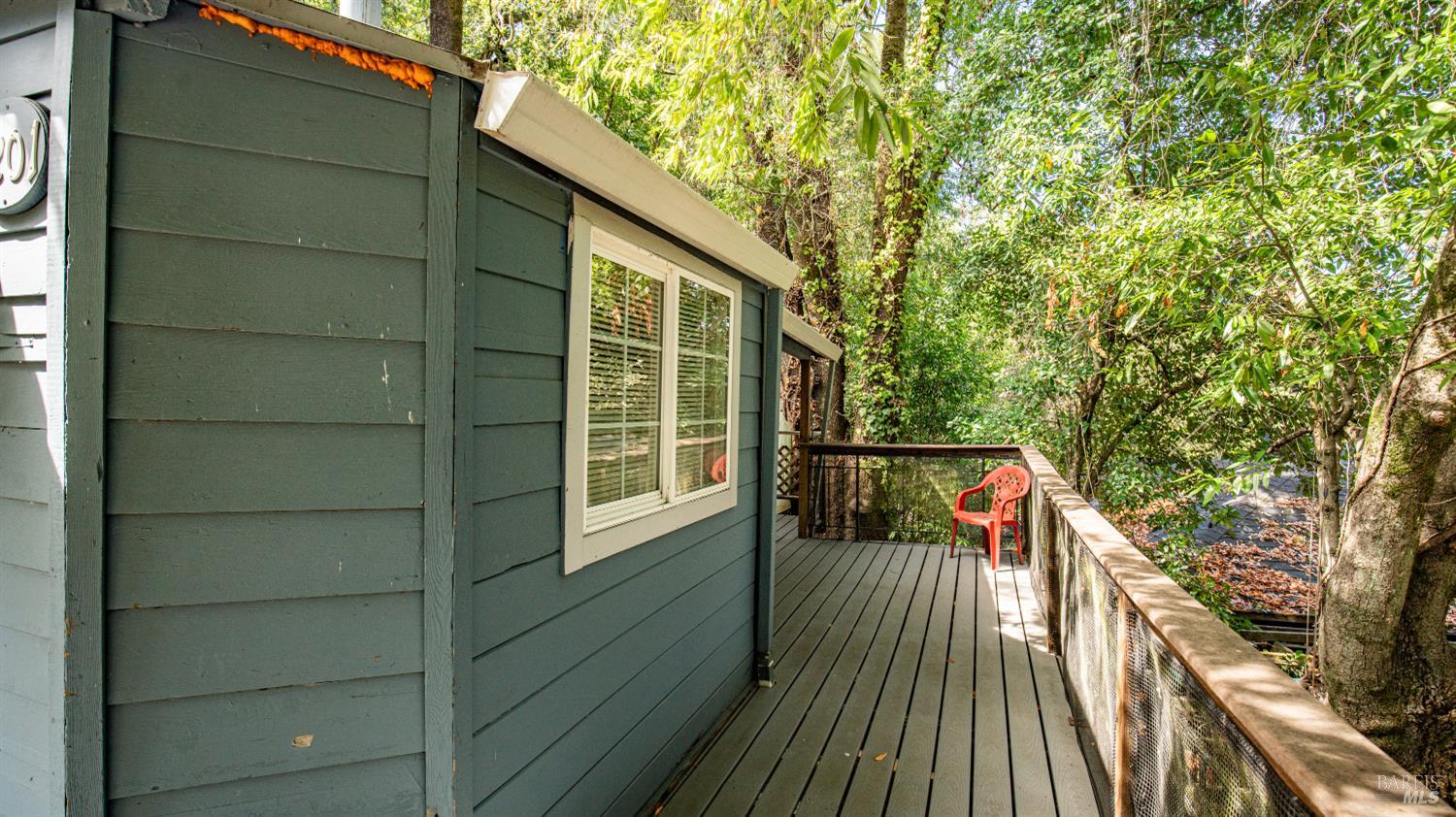Wooden deck beside a dark green home, with a red chair and wooded surroundings.