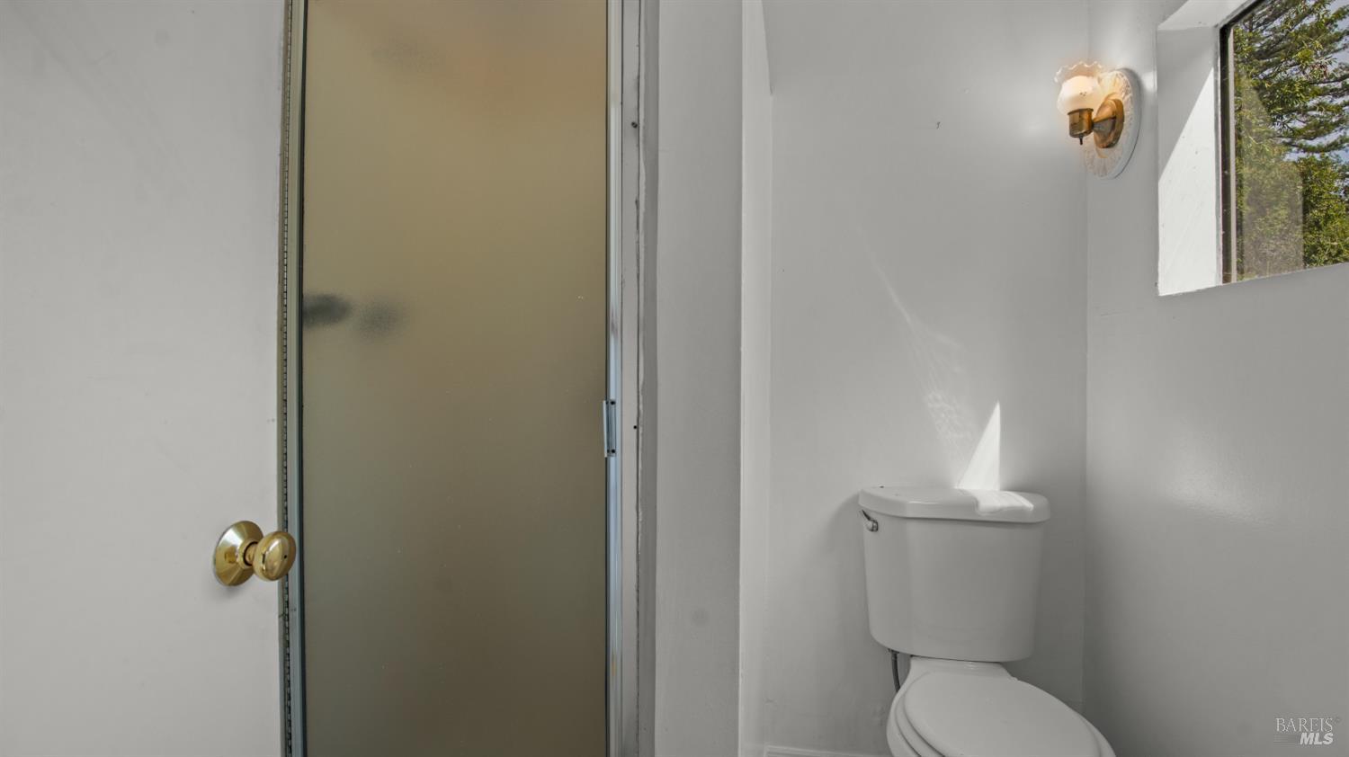 Bathroom with a frosted-glass shower stall, toilet, and high window.
